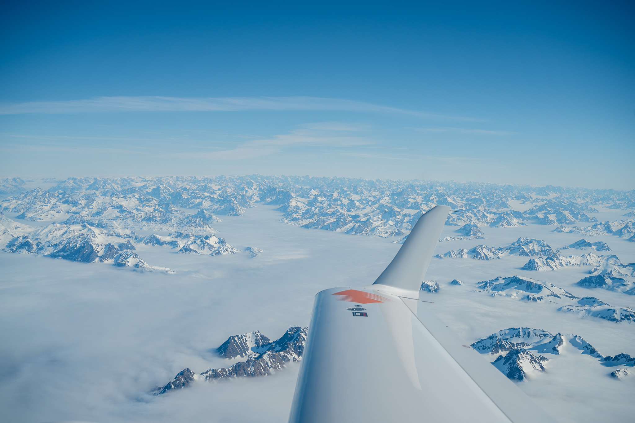 An aircraft wing above Greenland mountains and ice